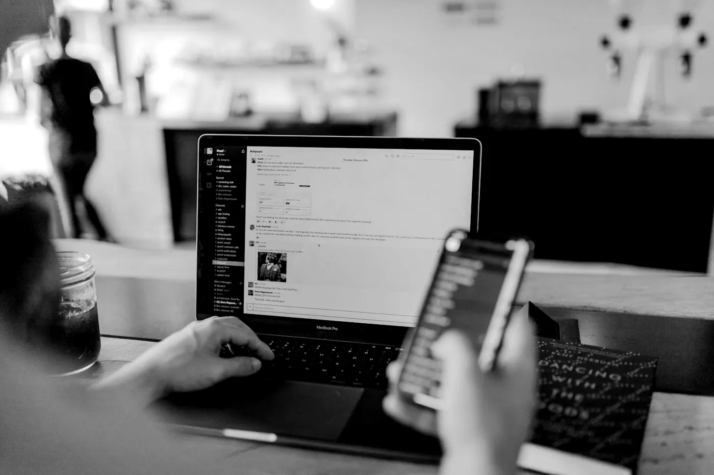 Persona revisando su teléfono frente a una computadora